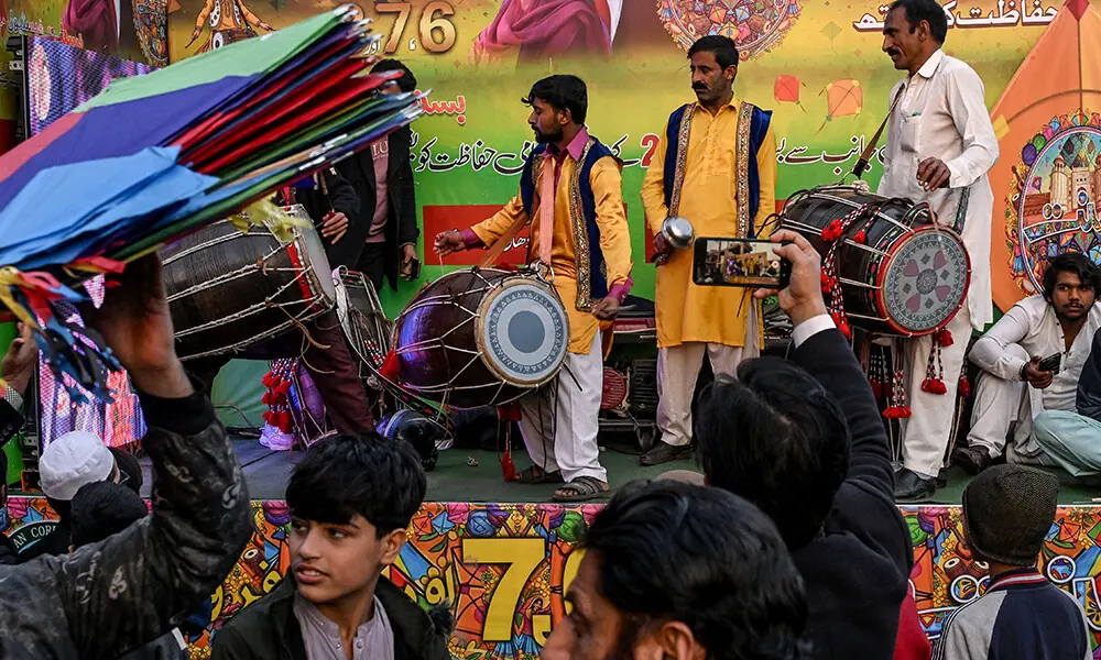 4 فروری 2026 کو لاہور میں بسنت فیسٹیول کے موقع پر دکاندار پتنگیں بیچ رہے ہیں، جبکہ فنکار روایتی ڈھول بجا رہے ہیں۔ تصویر: اے ایف پی
