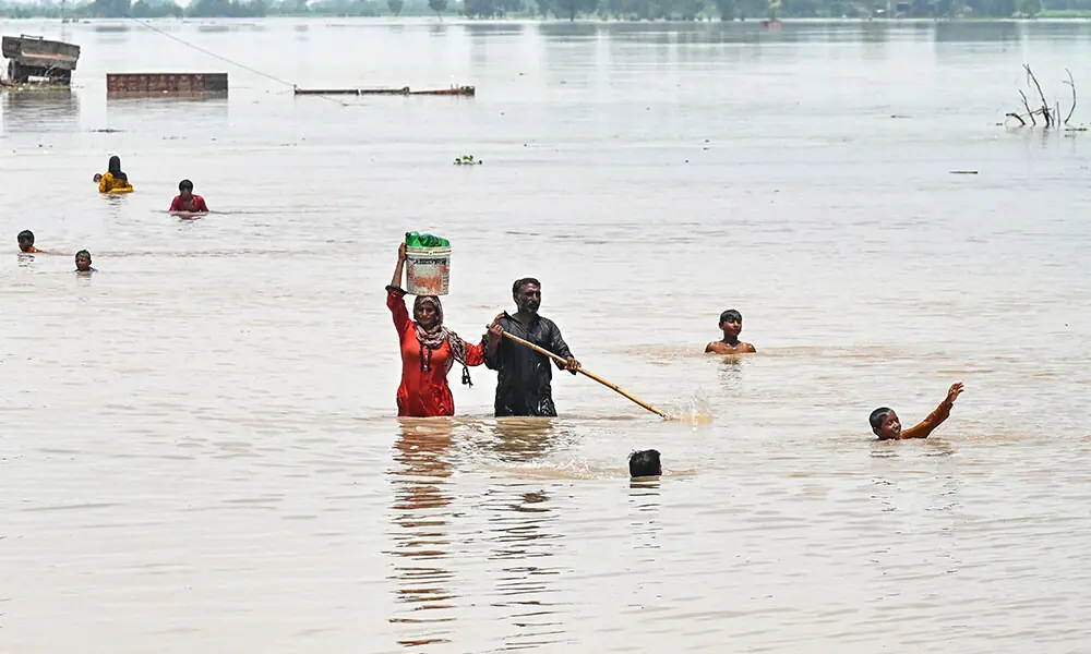People wade through a flooded area after heavy monsoon rains induced a rise in the water level of the River Ravi in Pakistan&rsquo;s Muridke on July 27, 2026. Photo: AFP