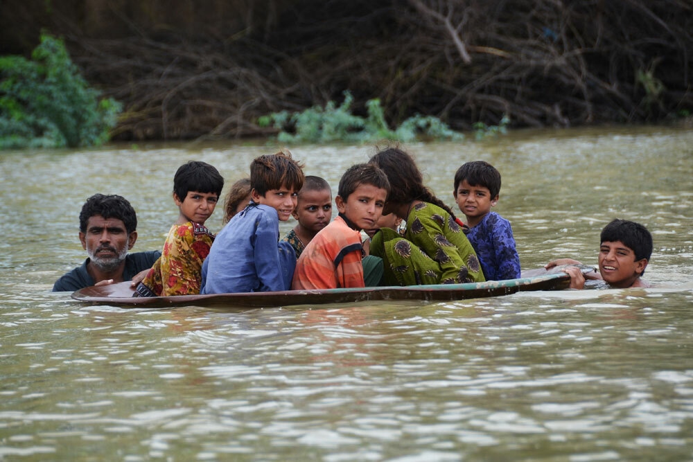 A man (L) along with a youth use a satellite dish to move children across a flooded area after heavy monsoon rainfalls in Jaffarabad district, Balochistan province, on August 26, 2022. - Heavy rain continued to pound parts of Pakistan on August 26 after the government declared an emergency to deal with monsoon flooding it said had "affected" over four million people. Photo: AFP