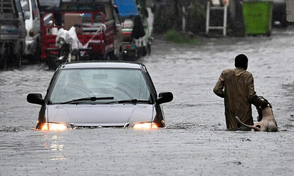 A man along with his dog while a car wade through a flooded street during heavy monsoon rains in Rawalpindi on July 17, 2025. Monsoon rains in Pakistan have been linked to more than 110 deaths including dozens of children since they arrived in late June, according to government figures released on July 14. Photo: AFP