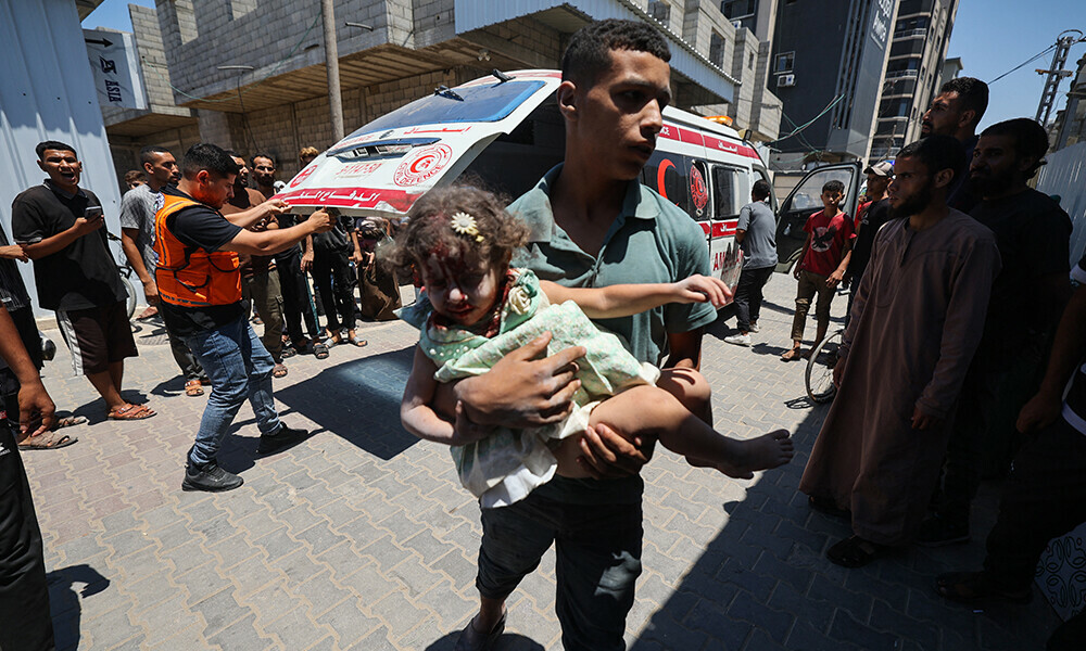 A Palestinian youth rushes a girl who was injured in an Israeli strike on an apartment at the Nuseirat refugee camp, into Al-Awda hospital in the central Gaza Strip on July 19, 2025. Photo: AFP