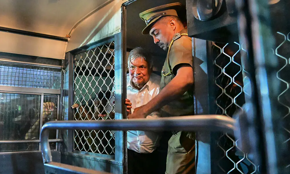 Sri Lanka&rsquo;s former president Ranil Wickremesinghe (L) is escorted to his seat in a prison bus in Colombo on August 22, 2025, after a magistrate ordered him to be held in remand custody till August 26, 2025. File Photo: AFP