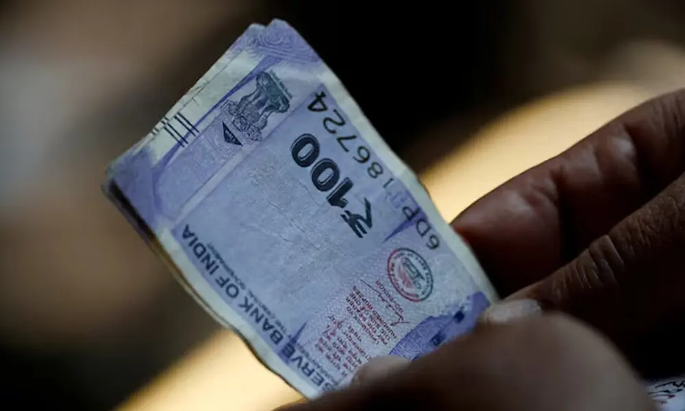A customer holds hundred rupees Indian currency notes near a roadside currency exchange stall in New Delhi, India, May 24, 2024. REUTERS