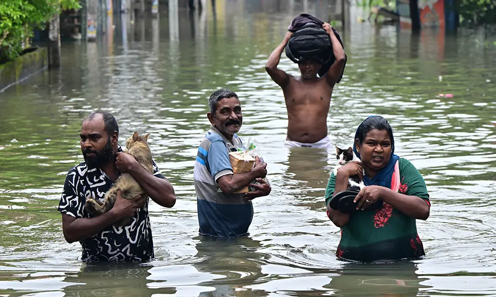 People wade through a flooded road after heavy rainfall in Wellampitiya on the outskirts of Colombo on November 29, 2025.