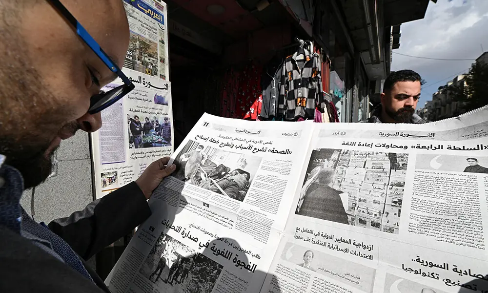 A man stands in the sun reading the &ldquo;Syrian Al-Thawra&rdquo; newspaper in Damascus on December 1, 2025. Photo: AFP