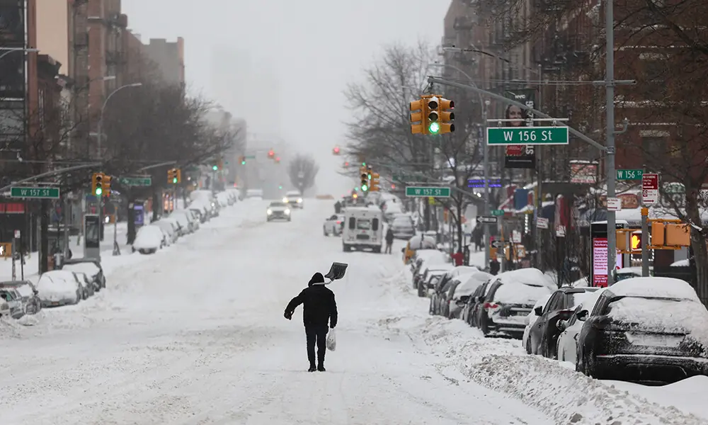 A man carries a shovel as he crosses a street in the Hamilton Heights neighborhood in New York on January 25, 2026.