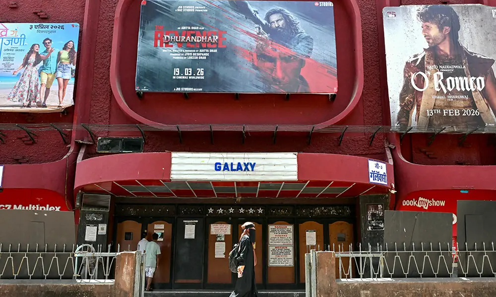 A woman walks past a poster of Indian Hindi-language spy action thriller film Dhurandhar: The Revenge (C), displayed outside a movie theatre in Mumbai on April 7, 2026. Photo: AFP