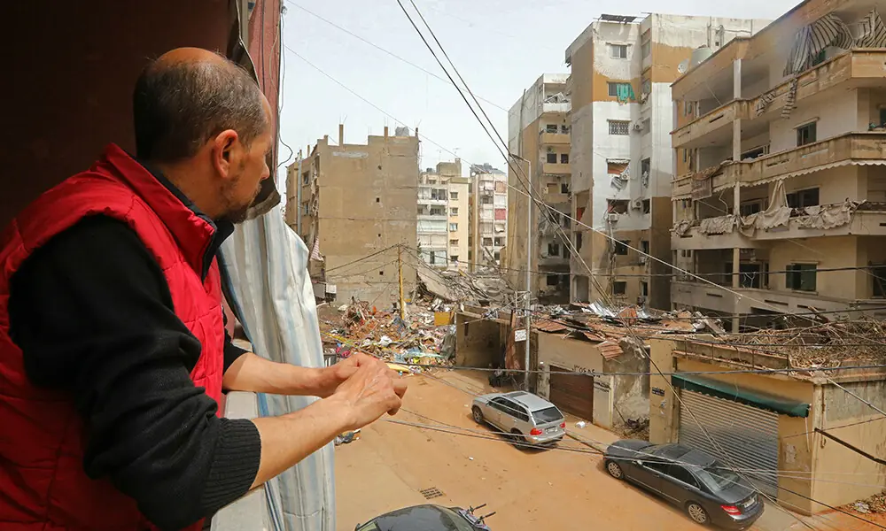 A resident watches the damaged buildings from the balcony of his house in a neighborhood of Beirut&rsquo;s southern suburbs, on April 18, 2026. Photo: AFP